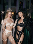 Two models in Pink Champagne and Black Eclipse silk lingerie styled as Glinda and Elphaba, with a crown, sheer cape, pointed hat and emerald-lined cape.
