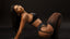 Model wearing black lingerie and stockings against a dark background